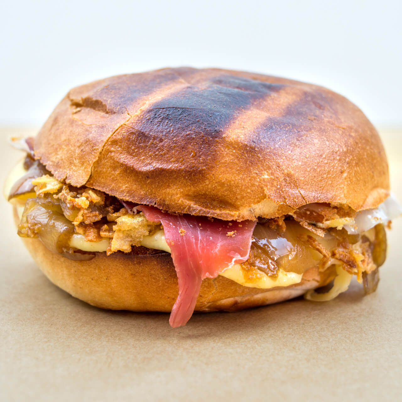 Bun au jambon cru, raclette et confit d'oignons
